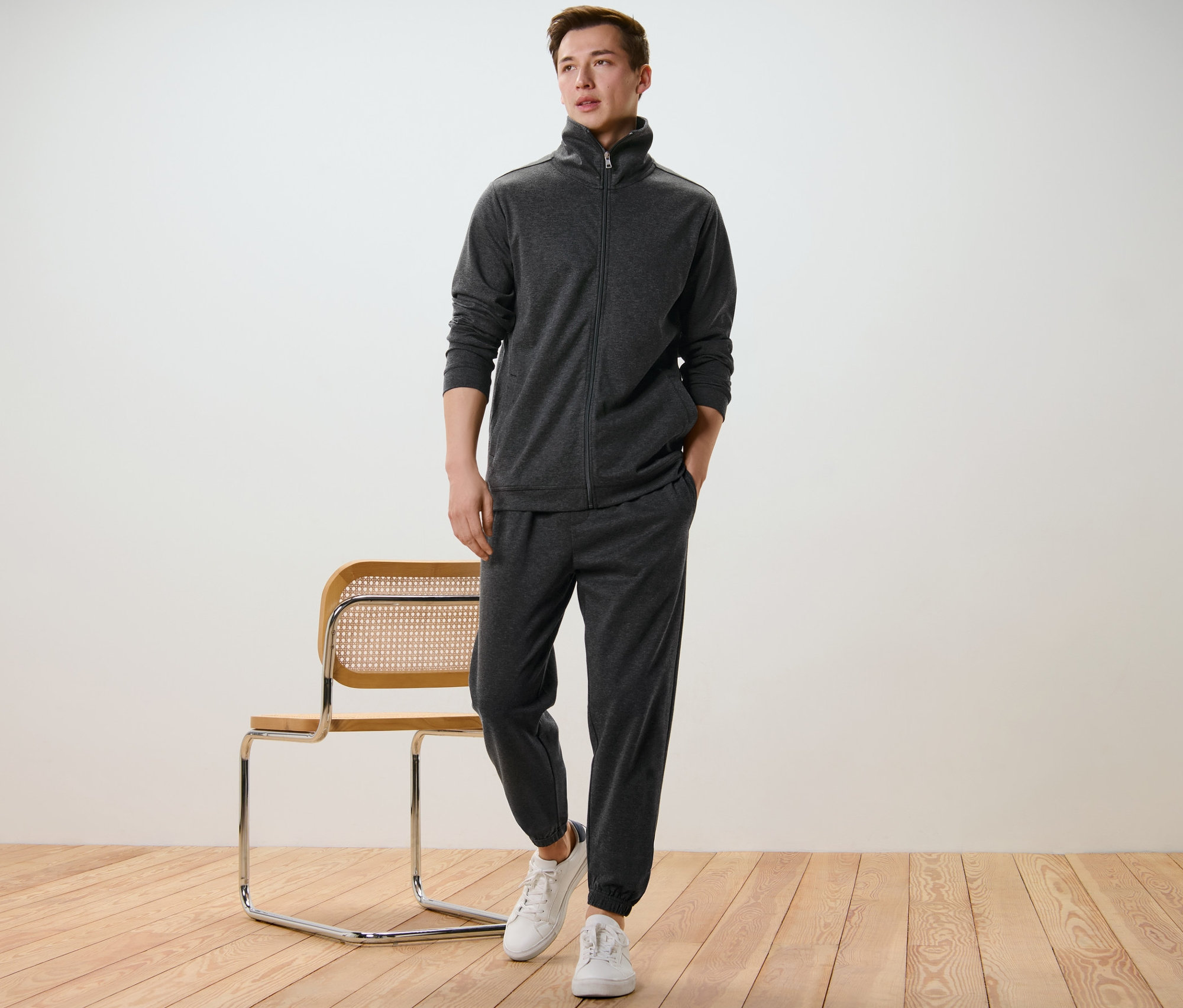 Mann posiert in Hausanzug und weißen Turnschuhen neben einem Stuhl.