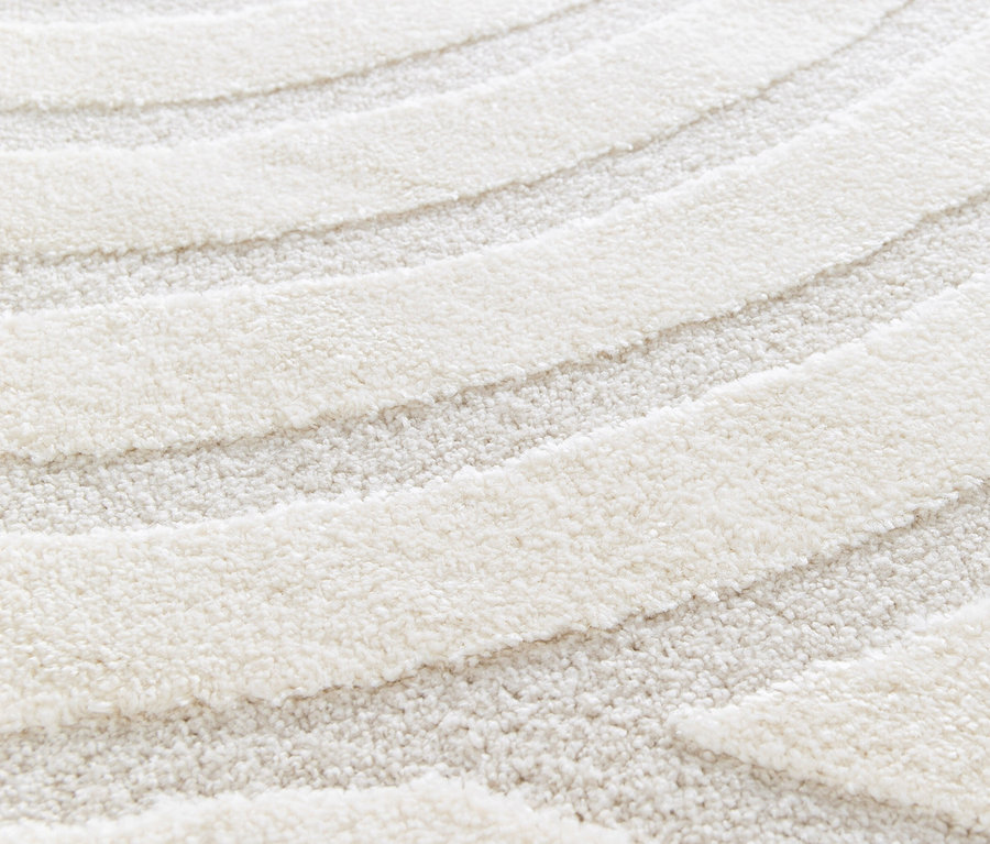 Nahaufnahme eines beigen Teppichs »Cosmo« mit gewelltem Muster.