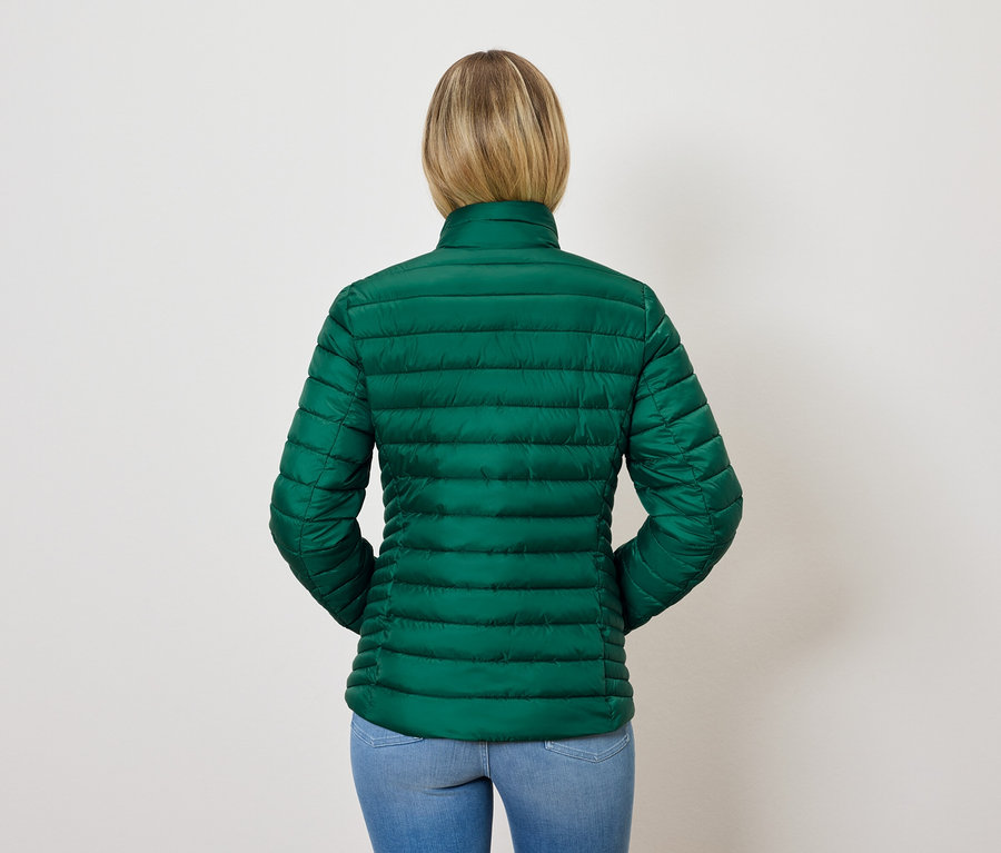 Rückansicht einer Frau mit blonden Haaren in einer grünen Steppjacke und blauen Jeans.