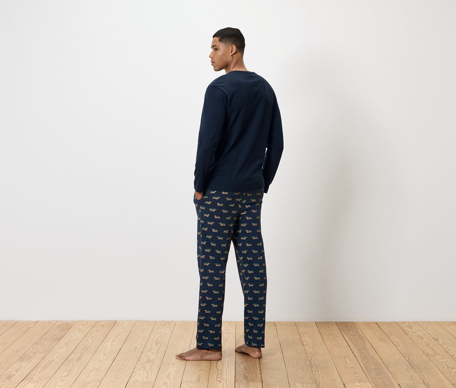Mann von hinten trägt einen dunkelblauen Schlafanzug mit Dackelprint.