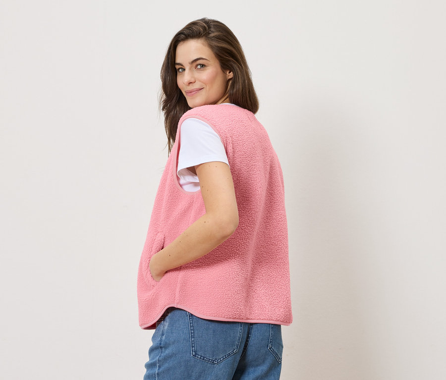 Frau blickt über die Schulter und trägt eine Teddy-Weste über einem weißen T-Shirt und Jeans.