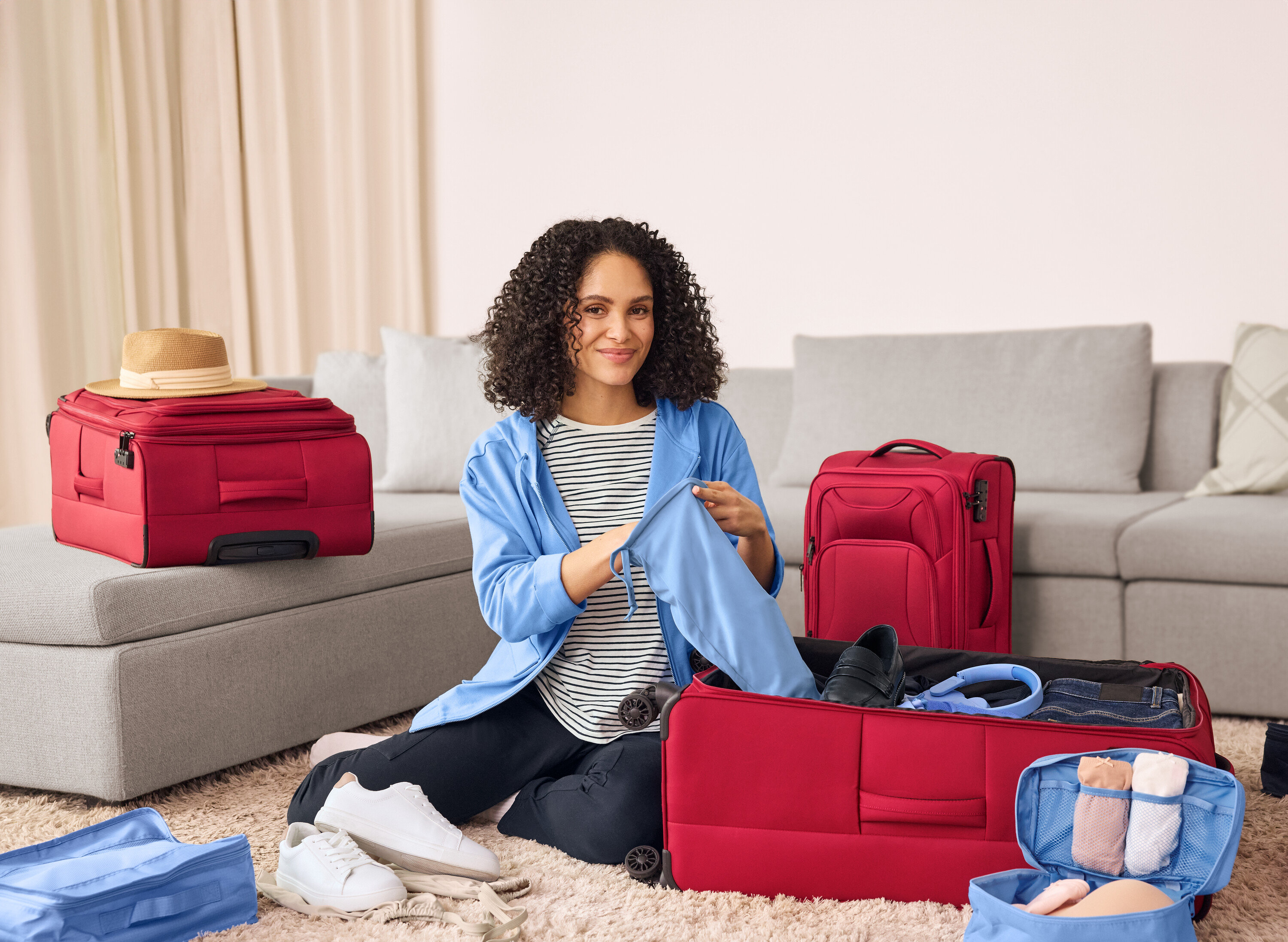 Eine Frau sitzt auf dem Boden und packt dunkelblaue Joggpants mit Cargo-Taschen in einen roten Koffer. Neben ihr stehen Leder-Sneaker.