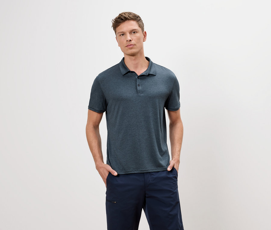 Mann mit blauem Poloshirt und blauen Shorts steht vor einem weißen Hintergrund.