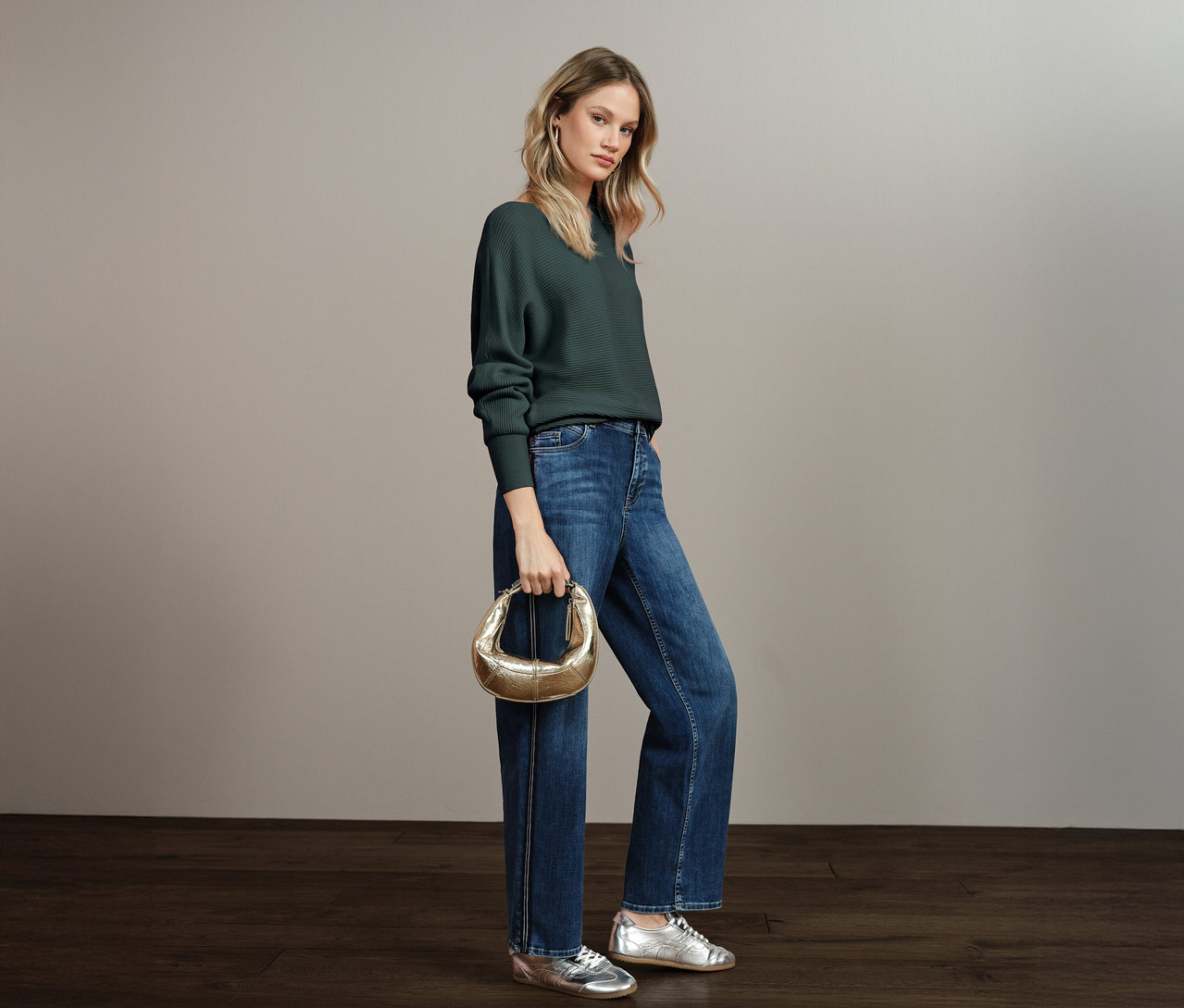 Frau trägt einen Street One Strukturpullover, Blue Jeans, silberne Schuhe und eine goldene Handtasche.