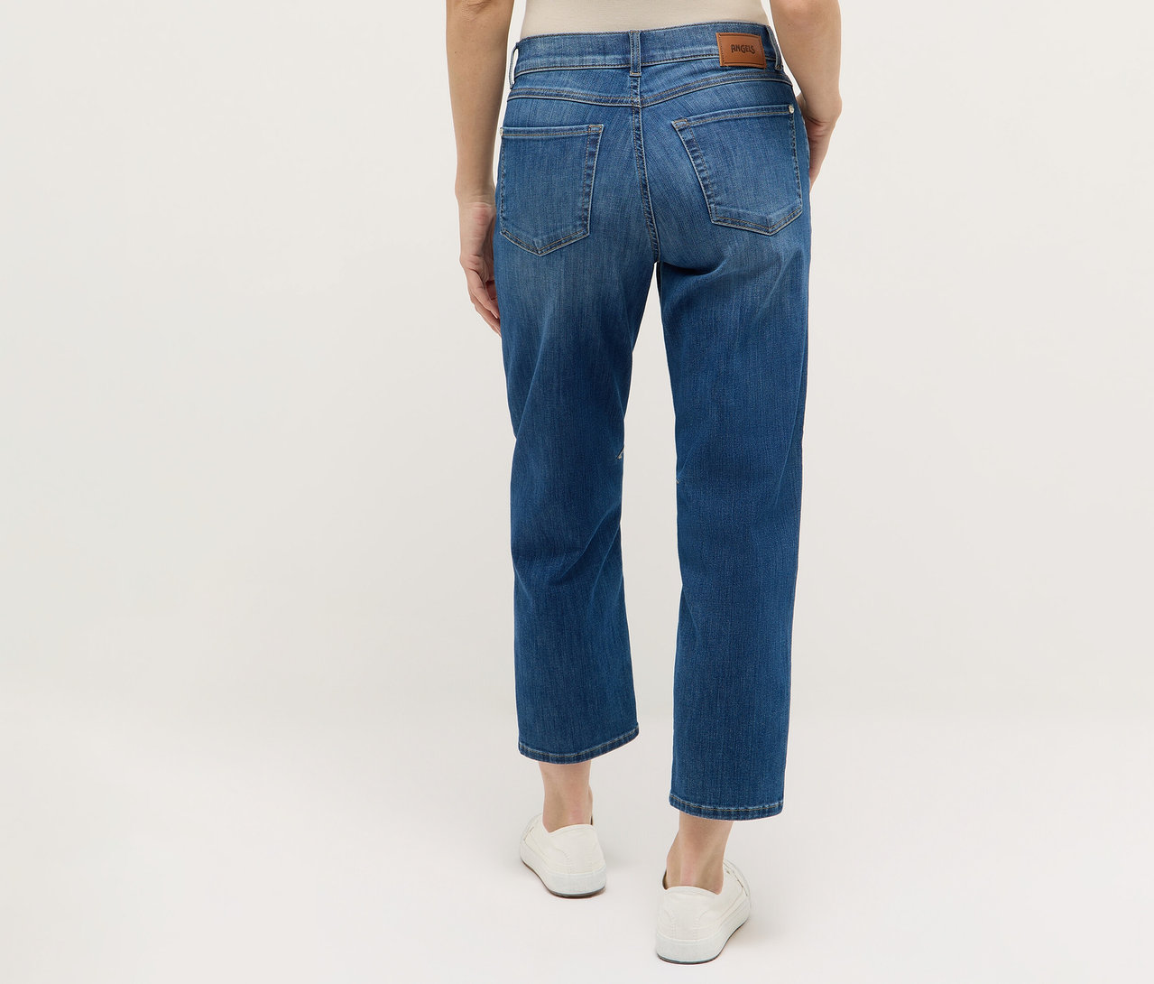 Rückansicht einer Frau, die blaue Angels Denim »Evi« Jeans und weiße Schuhe trägt.