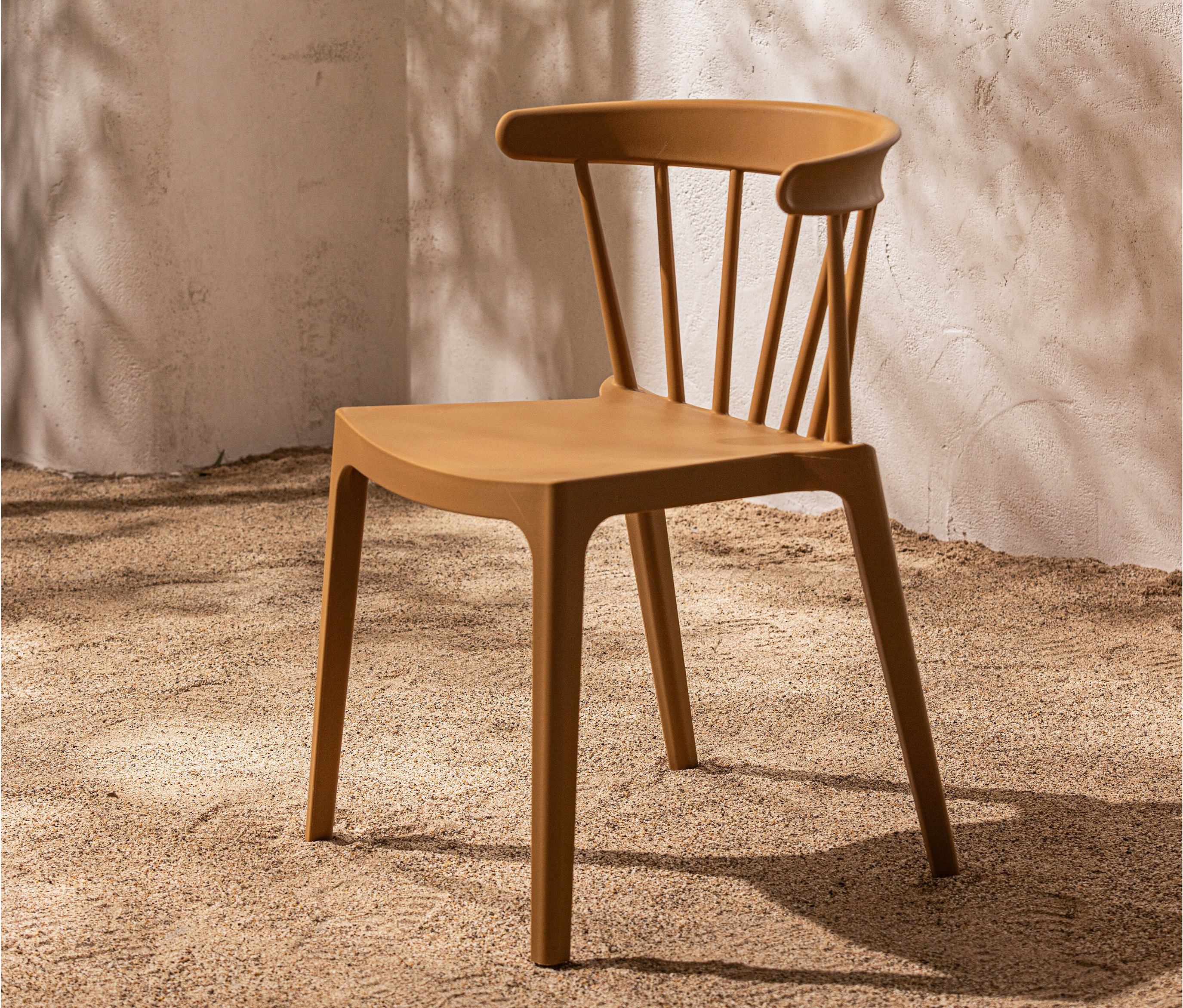 Ein einzelner senffarbener Stuhl steht auf sandigem Untergrund vor einer Wand.