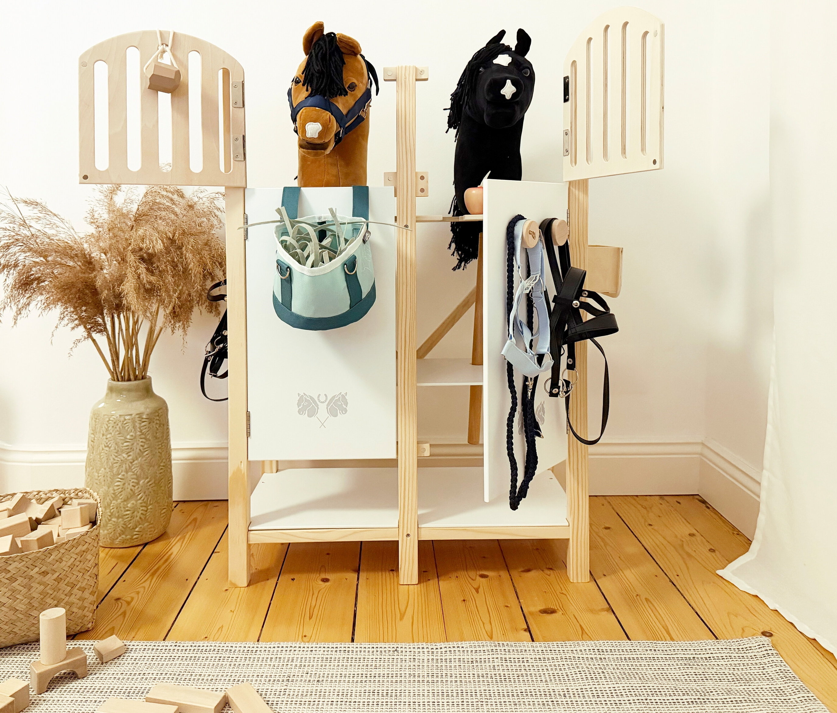 Zwei Steckenpferde stehen im small foot Hobby-Horse-Pferdestall mit Zubehör wie Trensen und Putztasche.