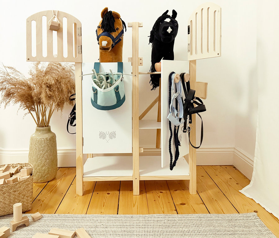 Zwei Steckenpferde stehen im small foot Hobby-Horse-Pferdestall mit Zubehör wie Trensen und Putztasche.