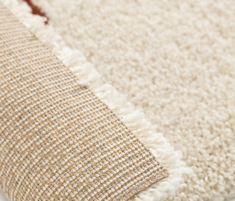 Nahaufnahme eines aufgerollten, cremefarbenen Shaggy-Teppichs mit Fransen.