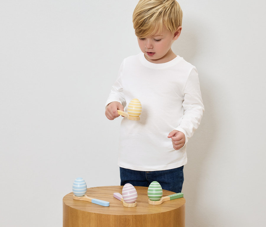 Ein Junge spielt mit bemalten Holz-Eiern und kleinen Hämmern auf einem Holztisch.