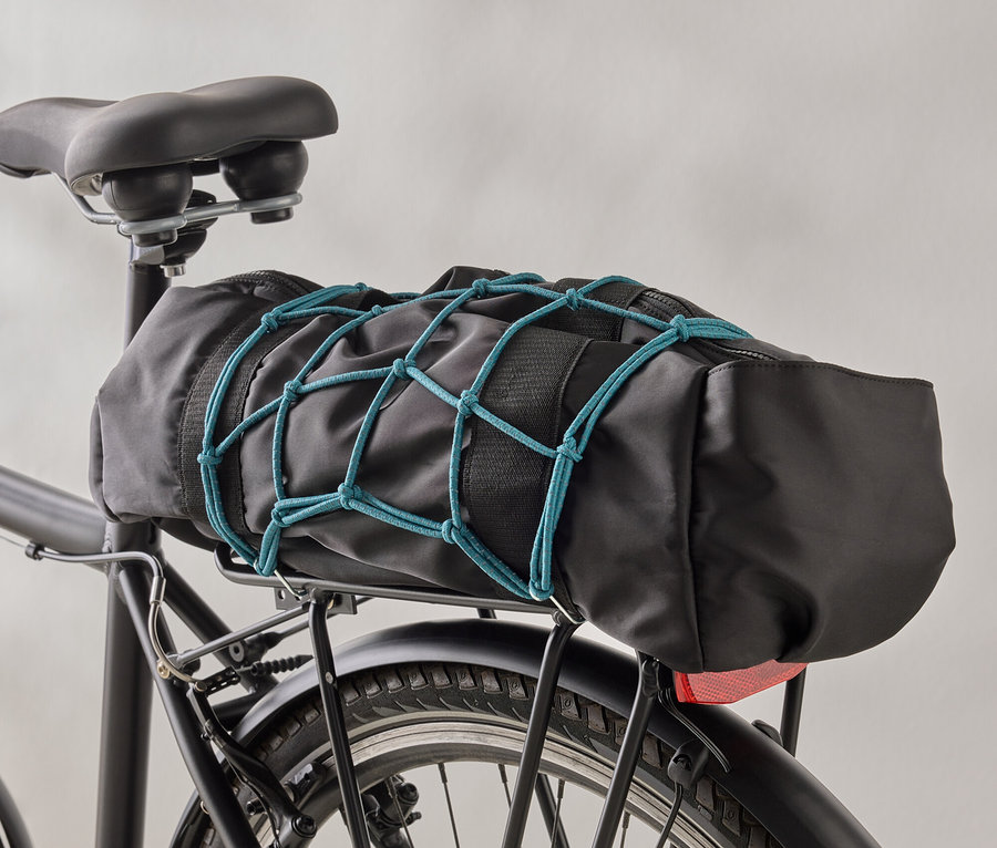 Eine schwarze Fahrradtasche ist mit einem blauen Gepäcknetz auf einem schwarzen Fahrradgepäckträger befestigt.