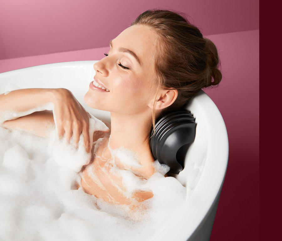 Frau lächelt und liegt in einer mit Schaum gefüllten Badewanne mit Badewannen-Massagekissen.