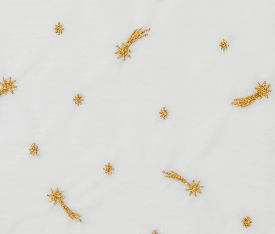 Detailansicht einer weißen Stoffoberfläche, bestickt mit goldenen Sternen und Kometen. Es handelt sich um eine Bistro-Gardine, bestickt.