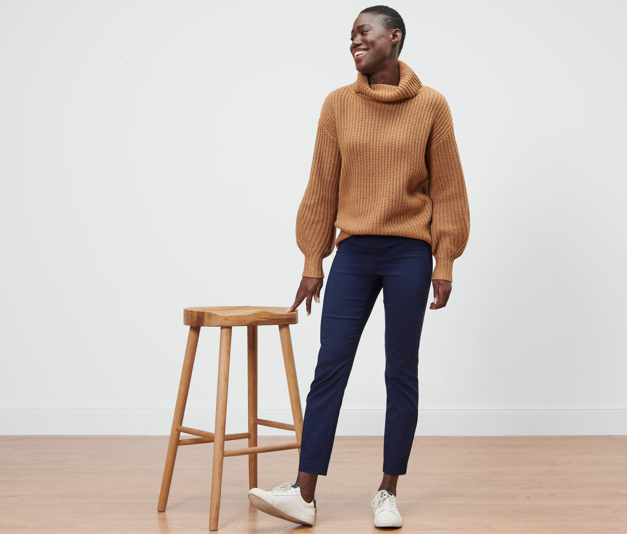 Frau steht neben einem Holzhocker und trägt eine blaue Stretchhose.