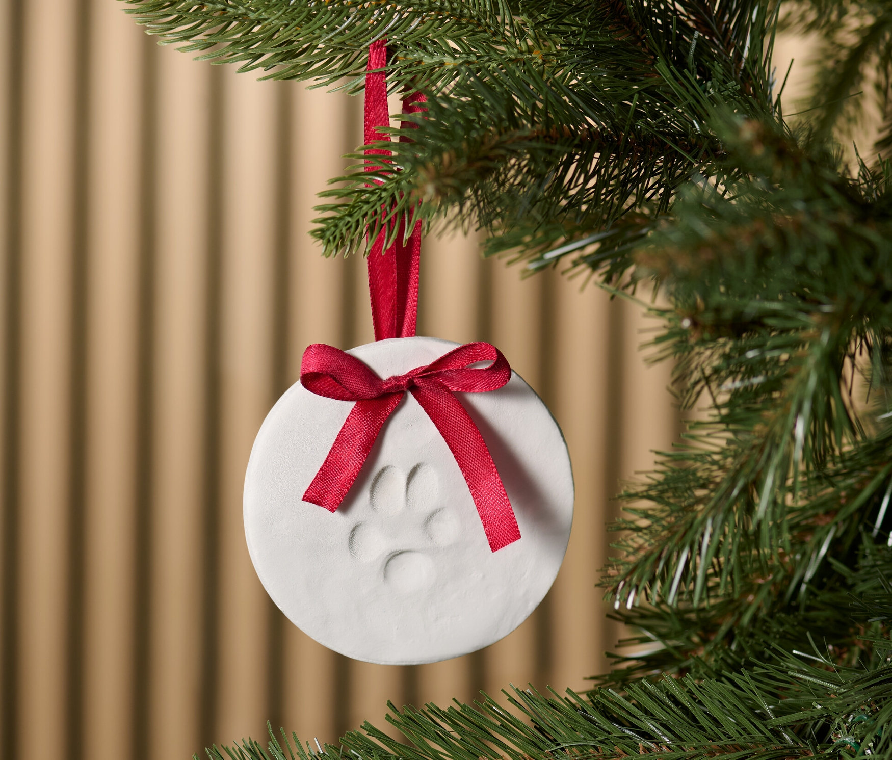 Pfoten-Abdruck-Set hängt an einem Weihnachtsbaum, geschmückt mit einer roten Schleife.