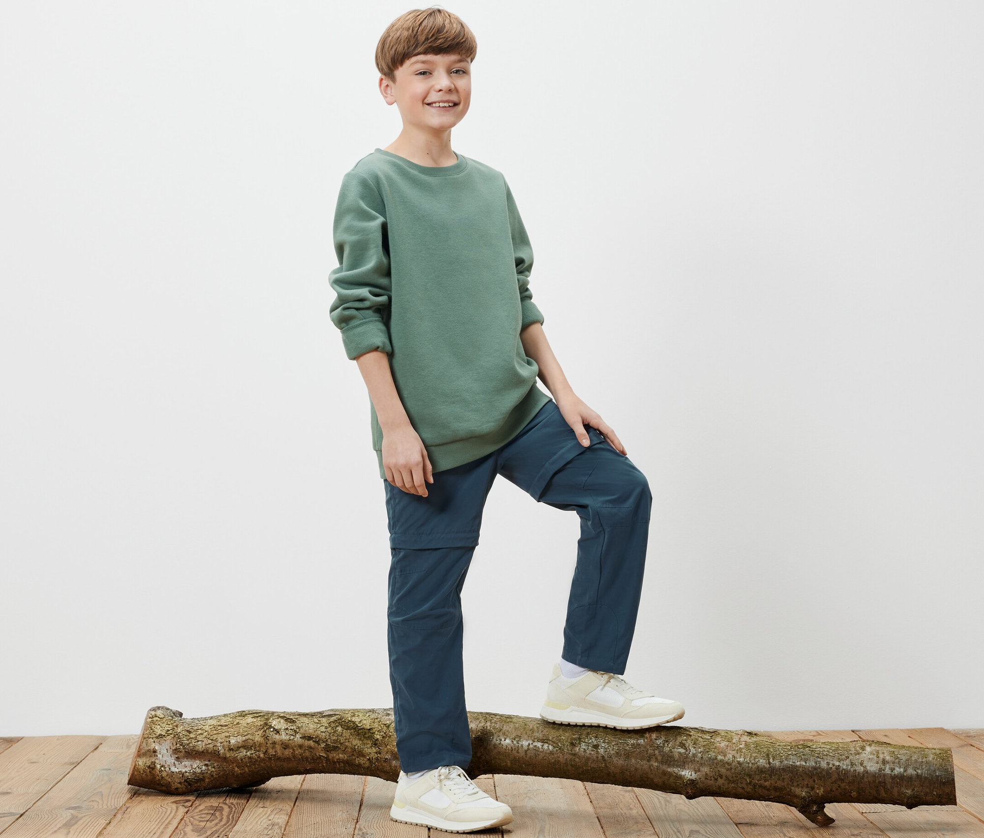 Ein Junge steht auf einem Baumstamm und trägt eine Kinder-Funktionshose.