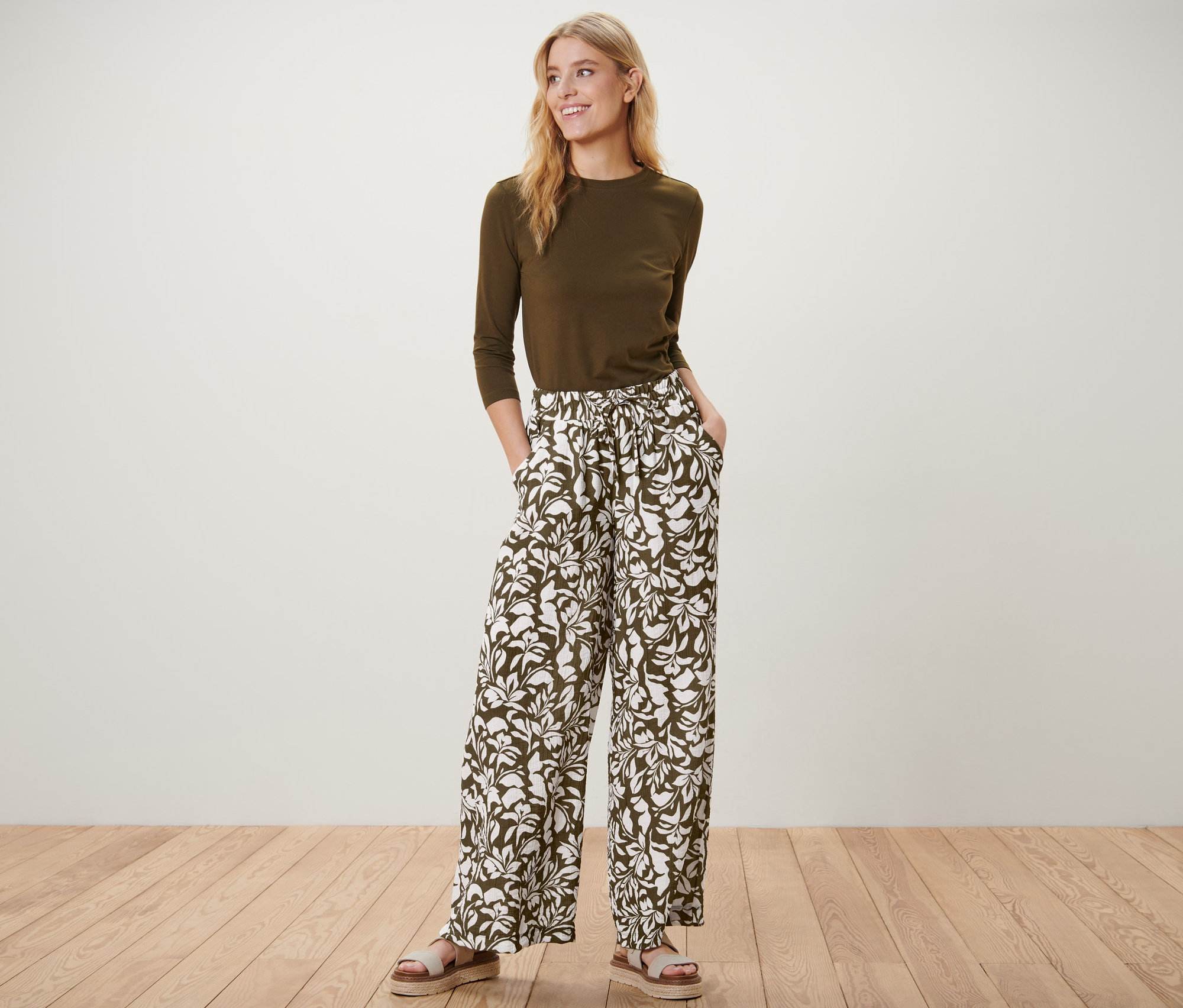 Frau posiert stehend in bedruckter Schlupfhose, olivgrünem Oberteil und Sandalen.