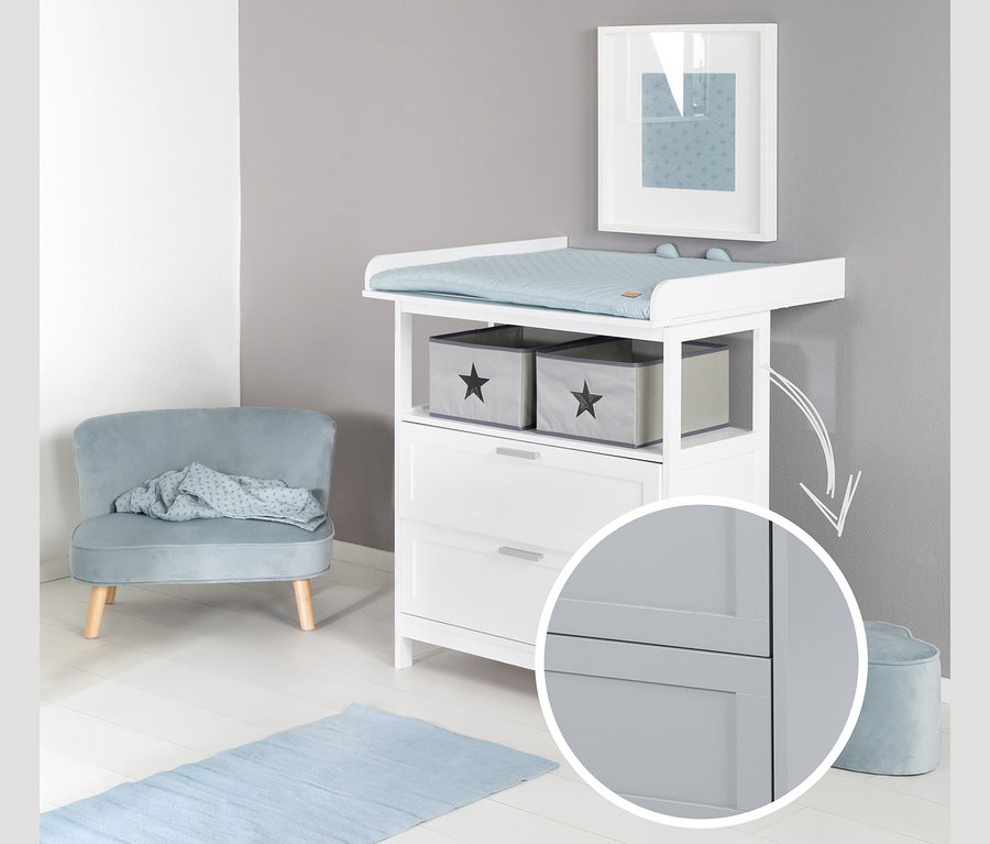Weiße roba Wickelkommode »Hamburg« mit Wickelansatz und blauer Unterlage. Im Hintergrund ein blauer Teppich und ein grauer Sessel.