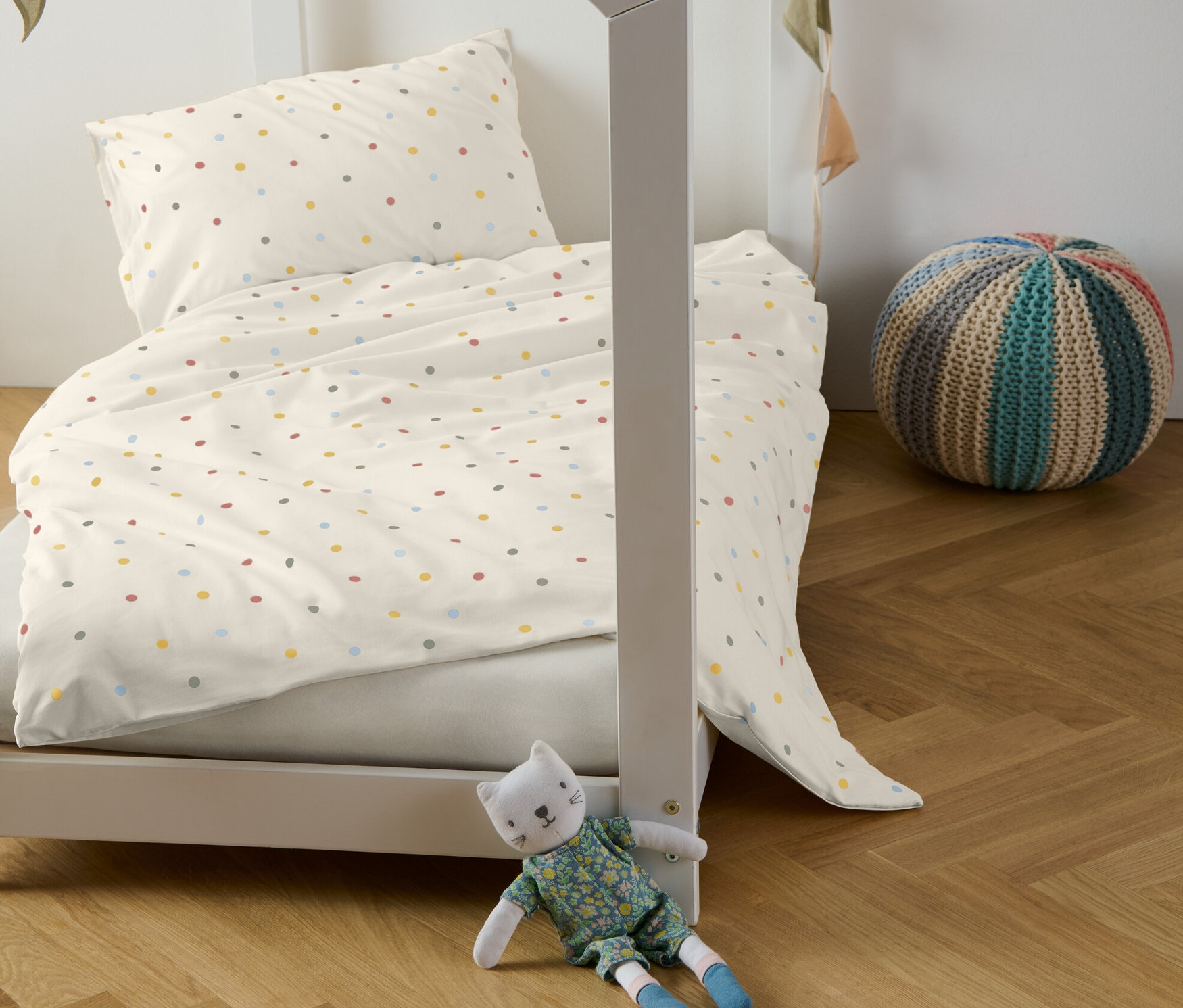 Kinderbett mit Kinder-Renforcé-Bettwäsche mit bunten Punkten, dekorative Girlande und Plüschkatze.