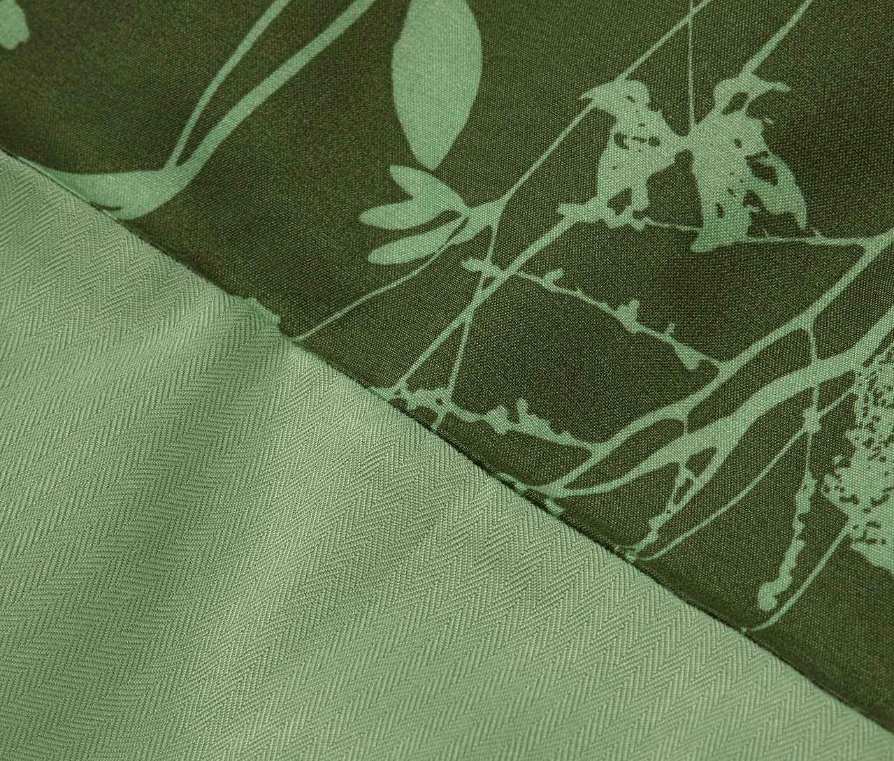 Detailaufnahme eines grünen Stoffes mit Blumenmuster und Fischgrätenmuster.