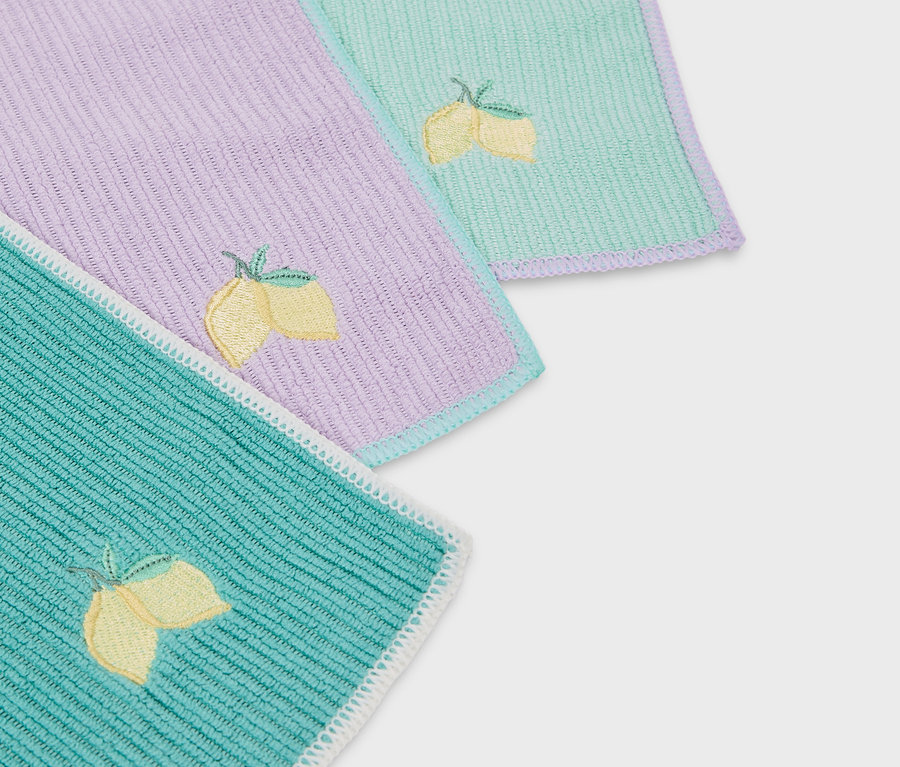 Detailaufnahme von drei farbigen Stoffservietten mit Zitronenstickerei.