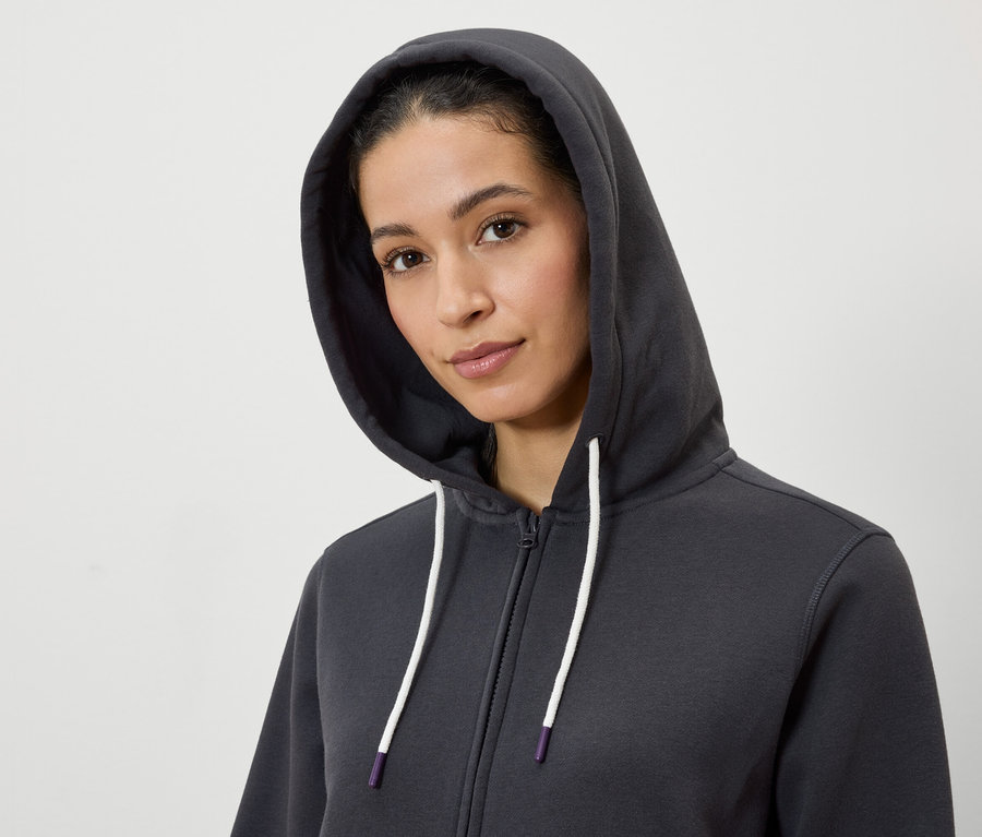 Porträt einer Frau mit Kapuze, die einen grauen Reißverschluss-Hoodie mit weißen Kordeln trägt.