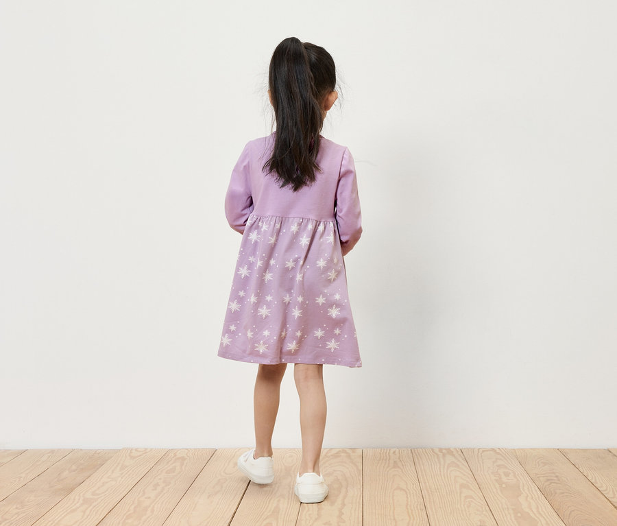 Mädchen in lila Kleid mit Sternen und weißen Turnschuhen steht mit dem Rücken zur Kamera.