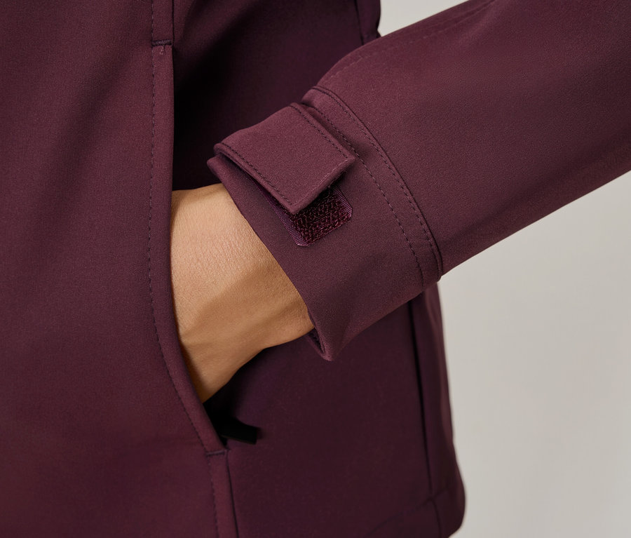 Hand in der Tasche einer weinroten Jacke, Details wie ein Klettverschluss am Ärmel.