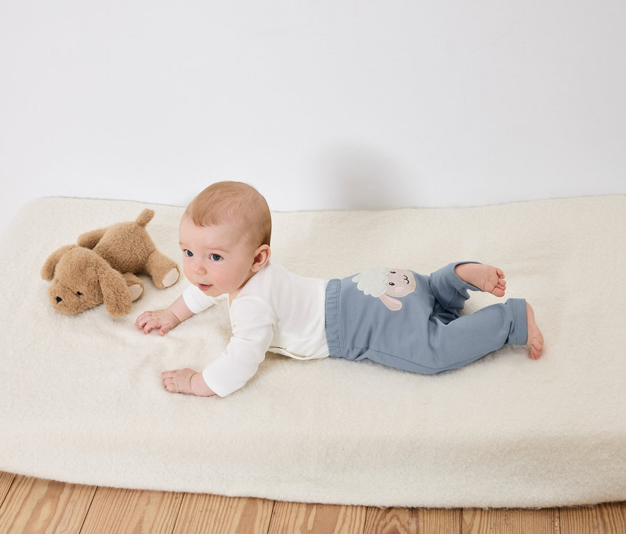 Baby liegt auf dem Bauch auf einer weißen Unterlage neben zwei braunen Stoffhunden.