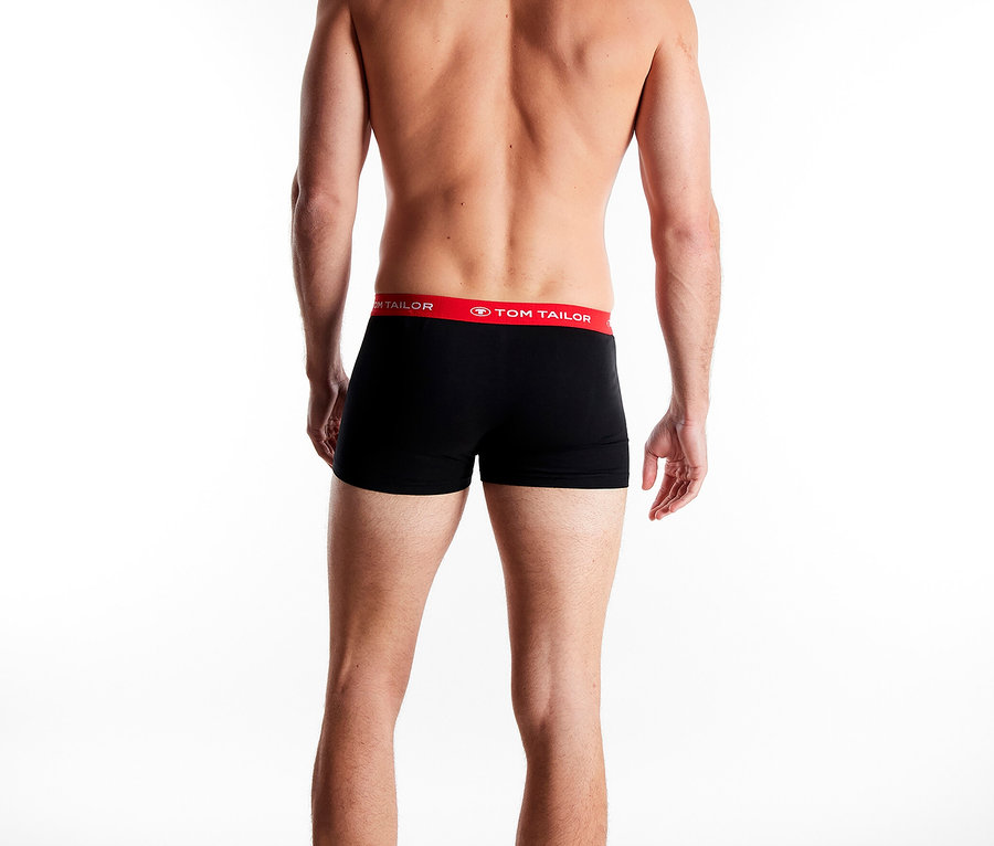 Rückansicht eines Mannes mit nacktem Oberkörper und schwarzen Tom Tailor Boxershorts mit rotem Bund vor einem weißen Hintergrund.