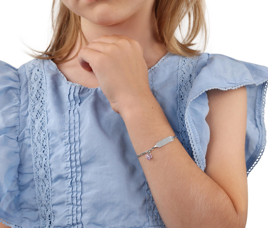 Nahaufnahme eines Mädchens in einem blauen Kleid, das ein silbernes Armband mit einem rosa Herzanhänger trägt.