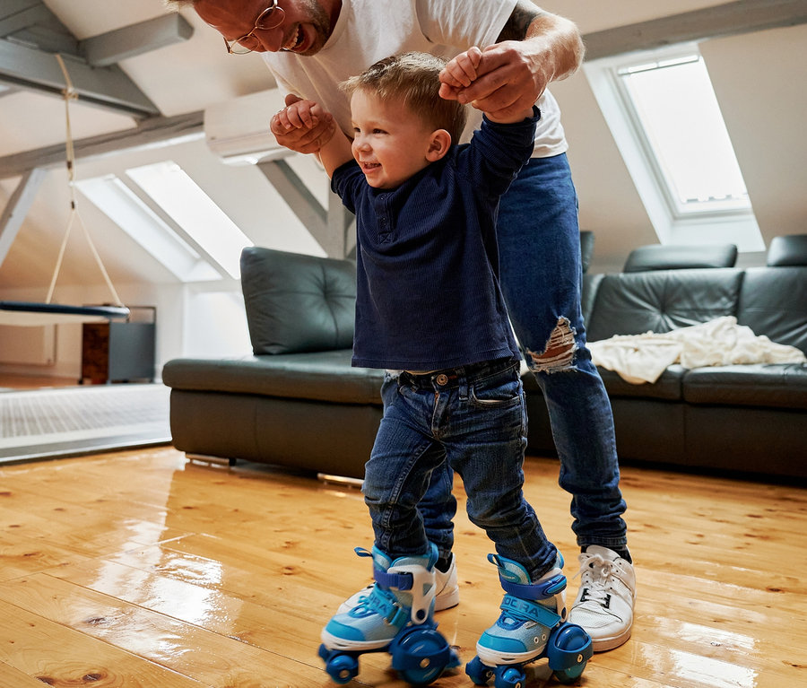 Vater bringt Sohn das Skaten auf blauen HUDORA My First Quad Rollschuhen bei.