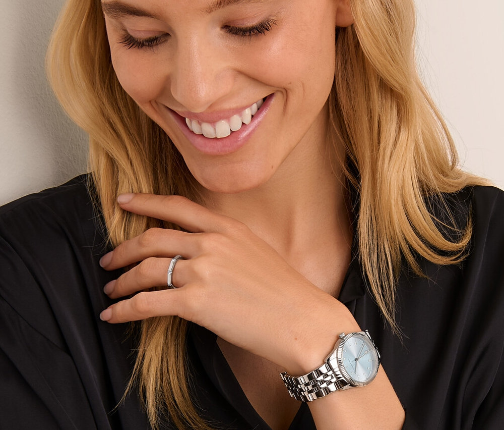 Lächelnde Frau schaut auf 925 Silber Ring Octagon und Edelstahl-Armbanduhr mit Datum.