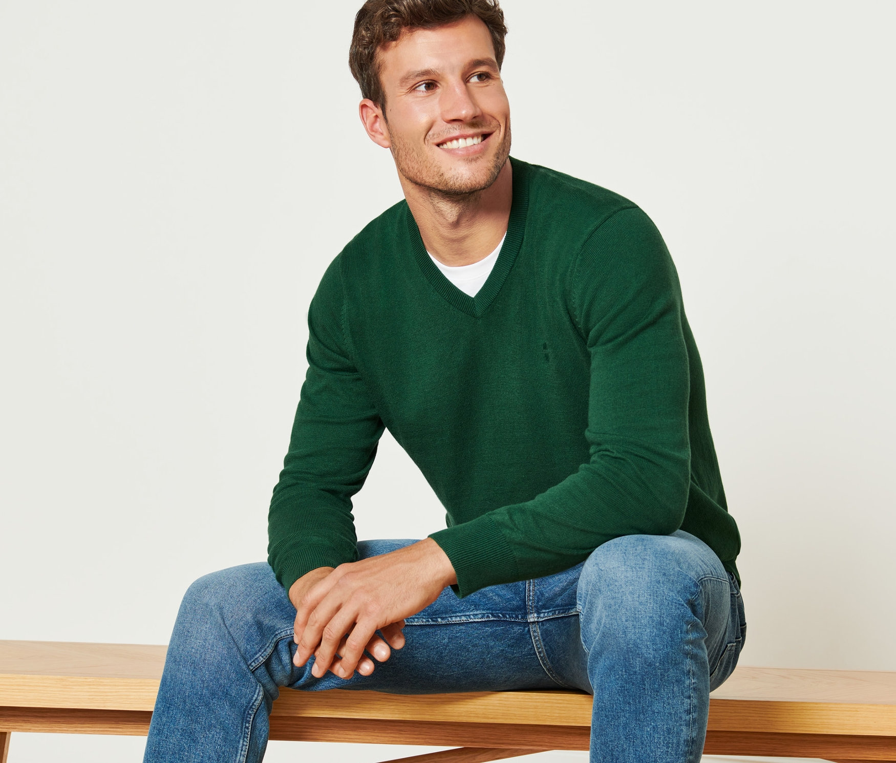 Ein Mann sitzt auf einer Bank und trägt einen dunkelgrünen Pullover mit V-Ausschnitt.