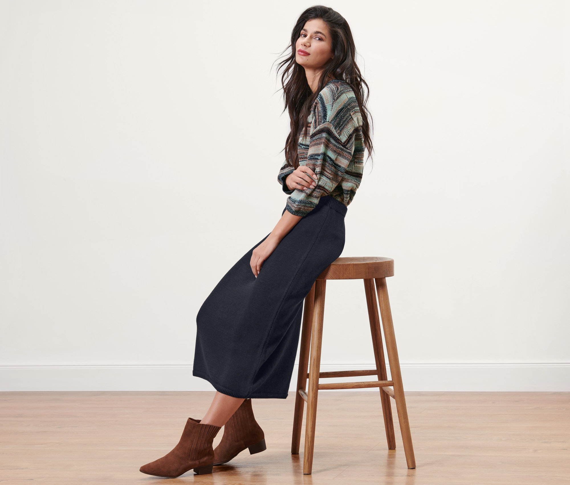 Brünette sitzt auf einem Hocker und trägt einen dunkelblauen Strickrock.