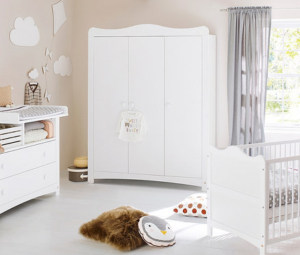 Kinderzimmer mit weißen Möbeln: Wickelkommode, Pinolino Schrank Florentina und Gitterbett. Auf dem Boden liegen ein braunes Fell und ein Kissen mit Pinguinmotiv.