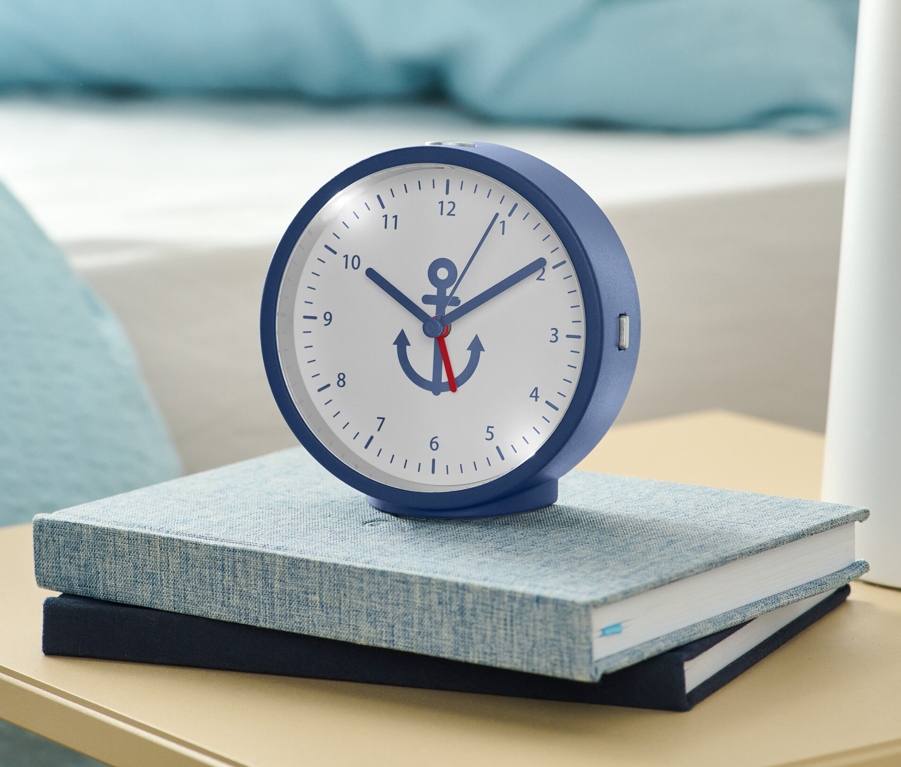Ein blauer Wecker mit Hintergrundbeleuchtung steht auf zwei Büchern auf einem Nachttisch.