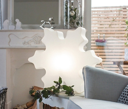 Innenaufnahme mit einem weißen Tisch, auf dem eine 60 cm große 8 seasons design LED-Schneeflocke steht. Neben dem Tisch steht ein grauer Sessel.