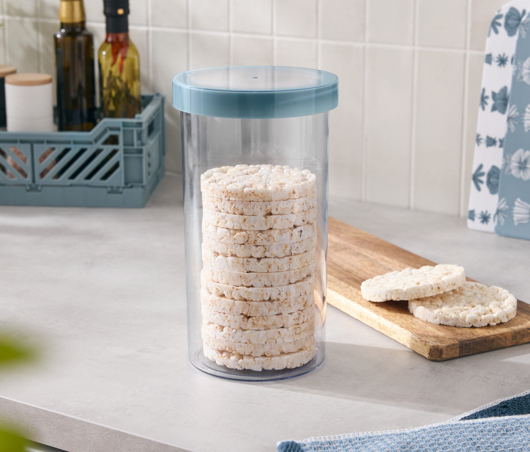 Reiswaffeln sind in einem Behälter mit blauem Deckel gestapelt, zwei weitere liegen auf einem Holzbrettchen.