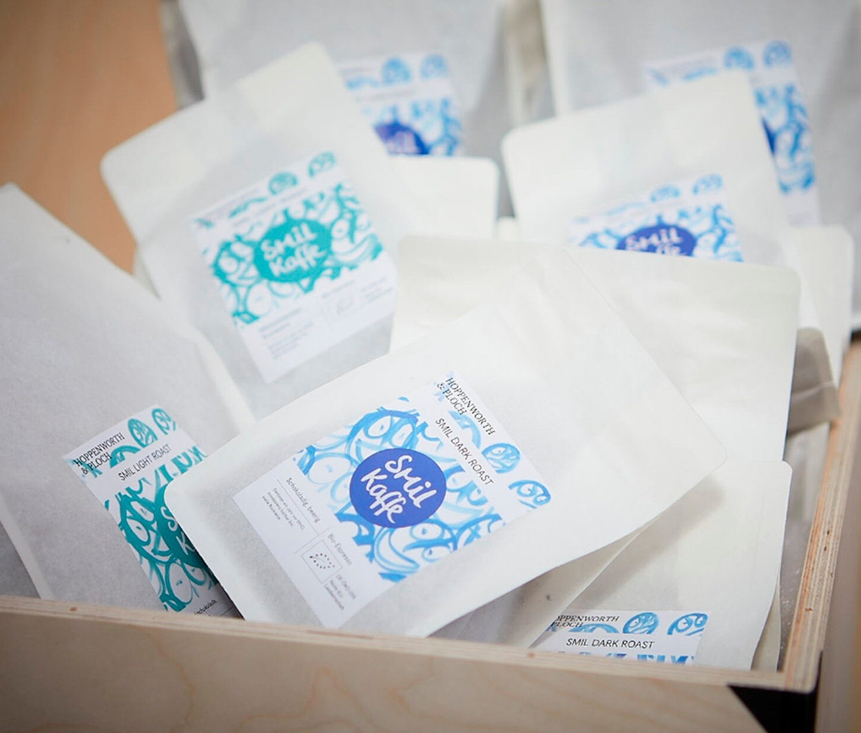 Ein Holzkasten gefüllt mit weißen Smil Kaffe-Kaffeetüten mit blauem Aufdruck.