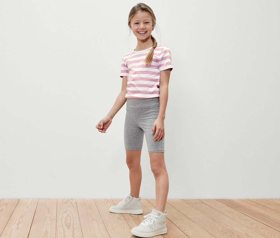 Lächelndes Mädchen posiert in grauen Kinder-Radler-Leggings und einem gestreiften T-Shirt.