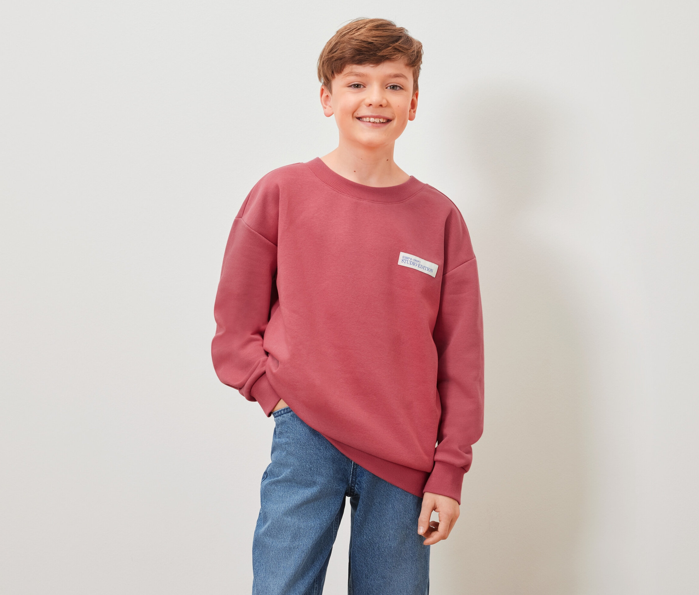 Junge posiert in rotem Kinder-Sweatshirt.
