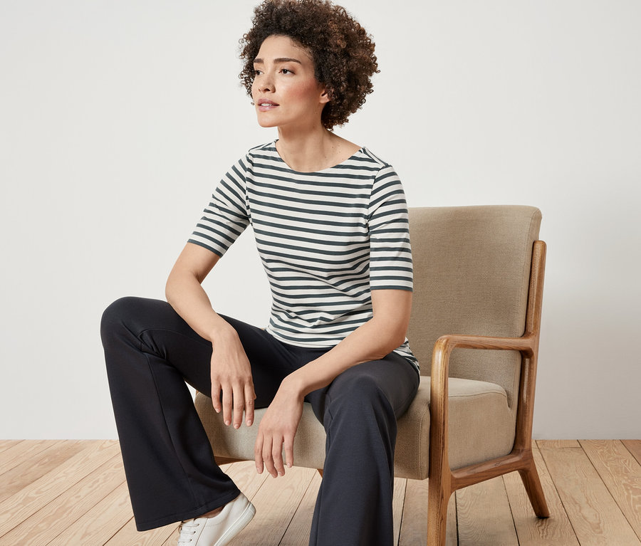 Frau sitzt auf einem Stuhl und trägt ein grün gestreiftes Halbarmshirt.