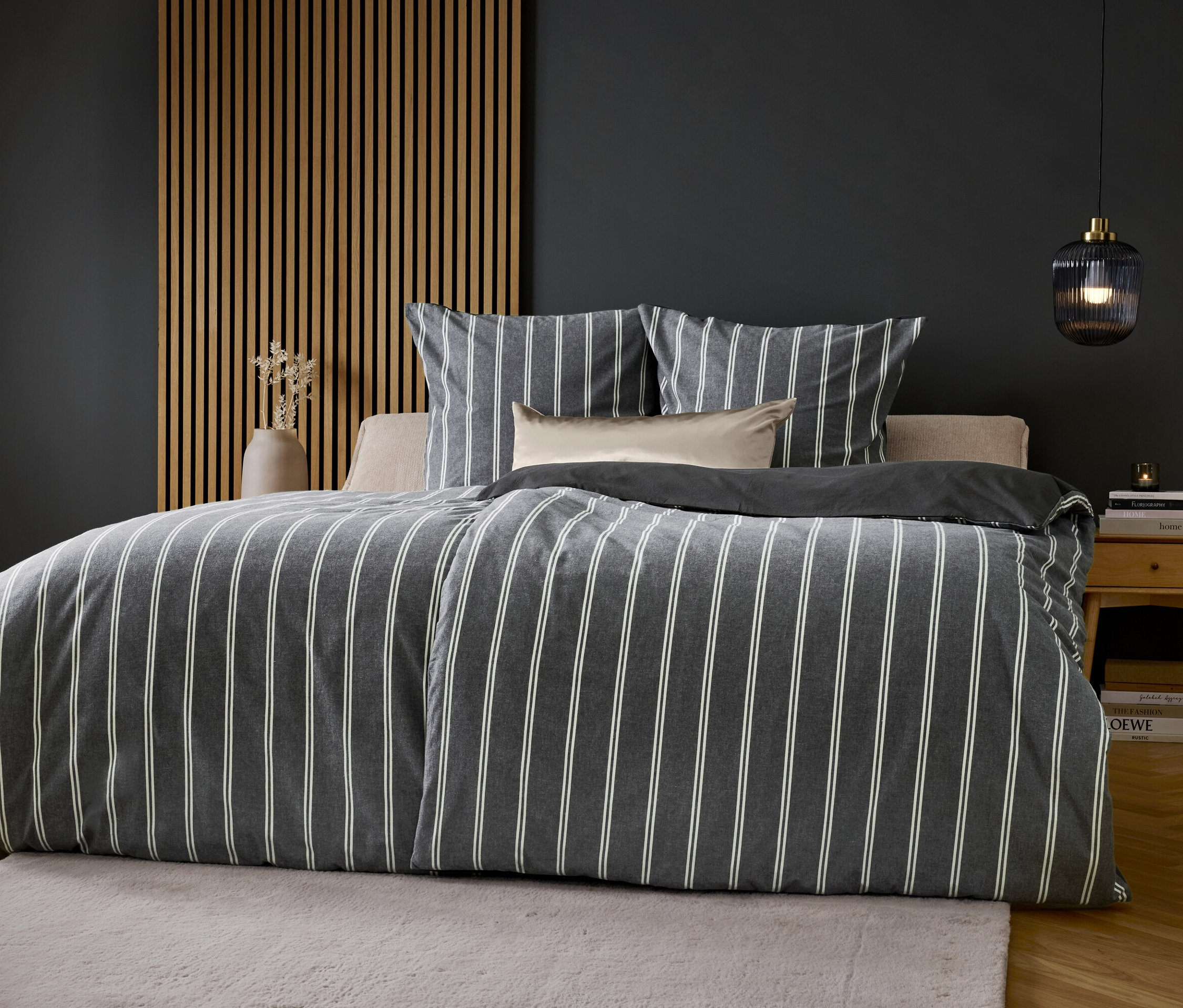 Ein Bett mit grau-weiß gestreifter Bettwäsche vor einer grauen Wand.