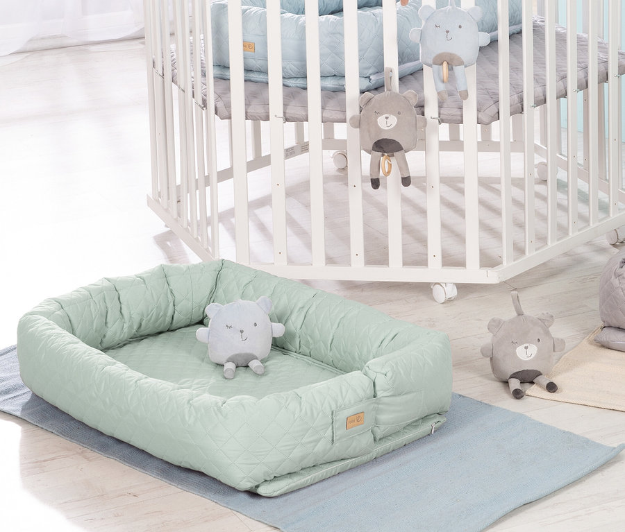 Grüne Roba 3-in-1 Babylounge mit Teddybär-Spielzeug liegt auf einer blauen Unterlage neben einem weißen Kinderbett.