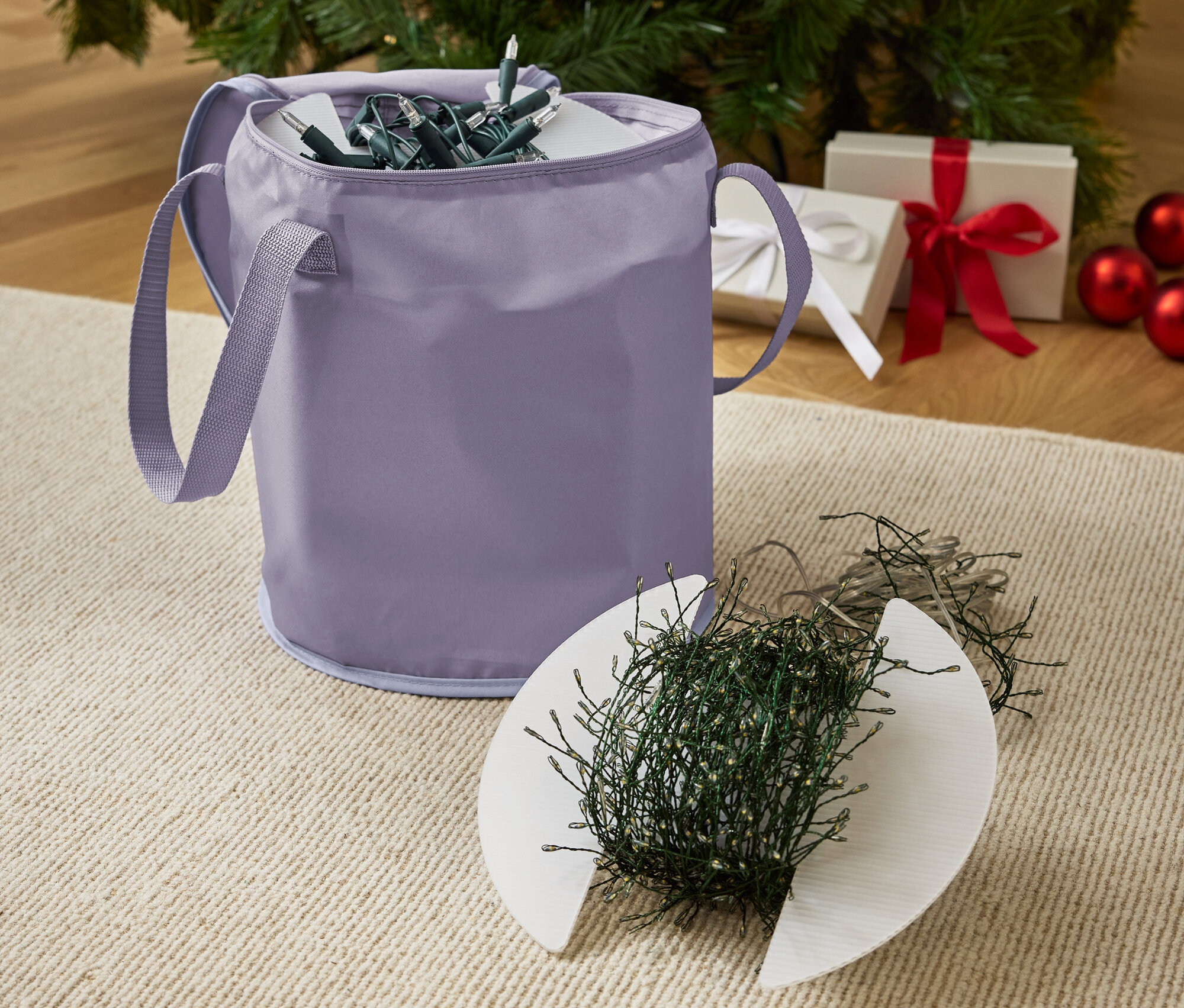 Ein lila Aufbewahrungskorb mit Weihnachtslichtern und ein geschmückter Weihnachtsbaum im Hintergrund.