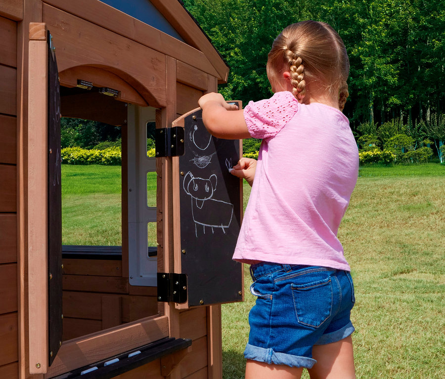 Mädchen zeichnet mit Kreide auf die Tafel des Spielhauses Trolli im Garten.