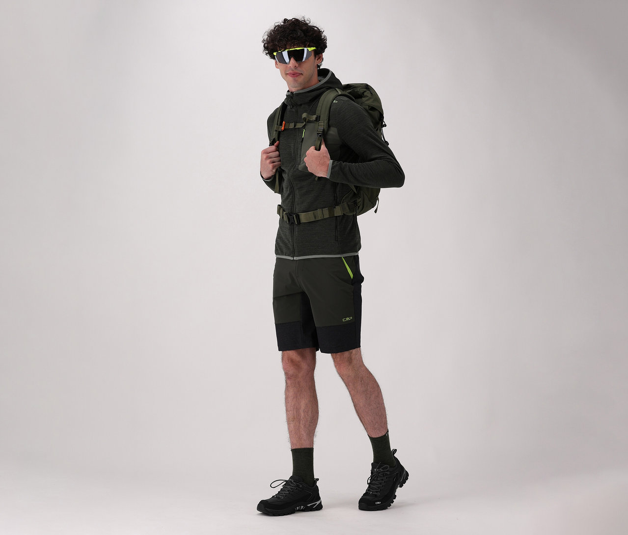 Mann mit Rucksack und CMP Herren-Trekkingschuhen RIGEL LOW 2.0 WP in Schwarz posiert vor hellem Hintergrund.