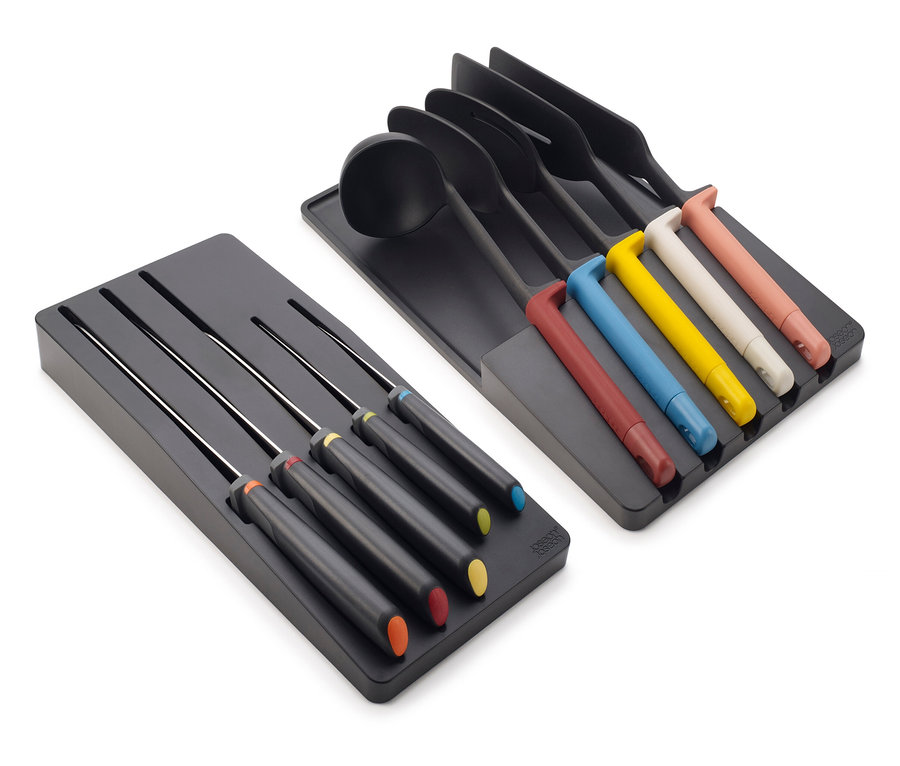Küchenhelfer und Messer mit farbigen Griffen liegen in schwarzen Schubladeneinsätzen.