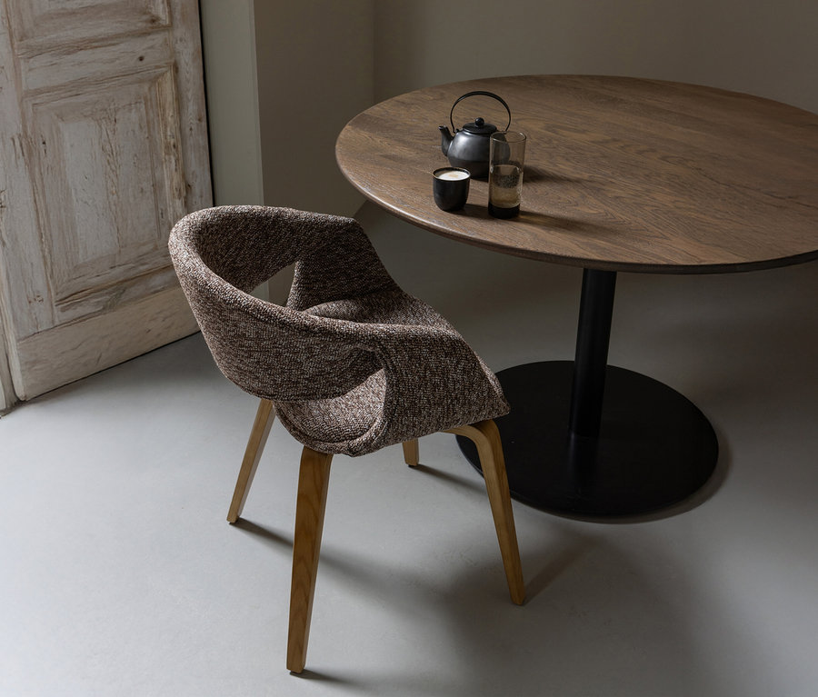 Ein brauner WOOOD Esszimmerstuhl »Yossi« mit naturfarbenem Holzfuß steht an einem runden Tisch mit Teekanne und Gläsern.